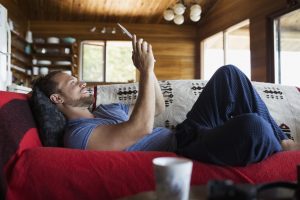 man laying down in his couch holding a tablet | sustainable new home